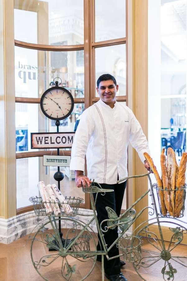 Chef Sameer Farhad Sehgal at a brasserie entrance with a bicycle of baguettes