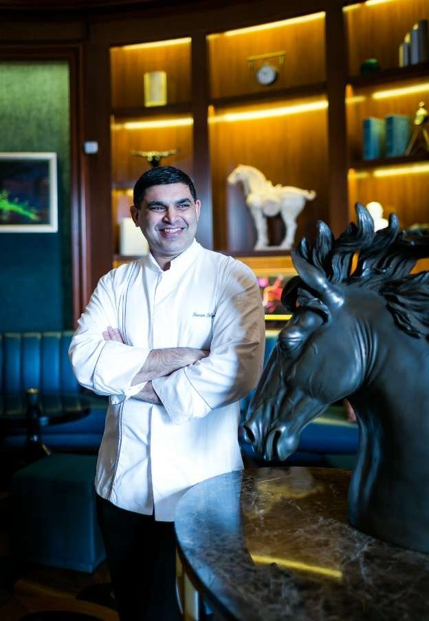 Chef Sameer Farhad Sehgal in a chef coat, standing in a wood-panelled lounge